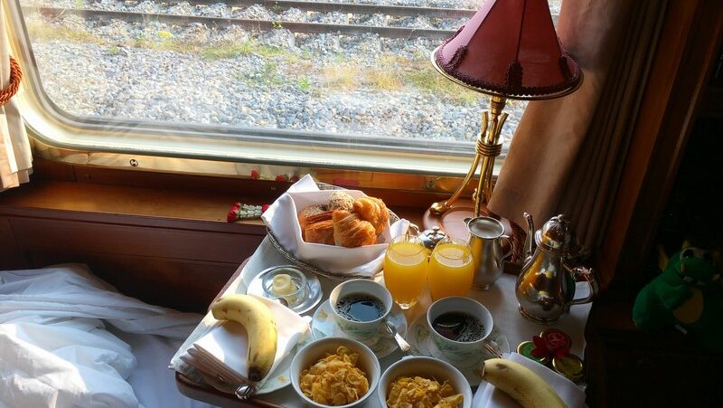 Frühstück am Bett im Zug mit Orangensaft, Kaffee, Croissants, Cornflakes und Bananen