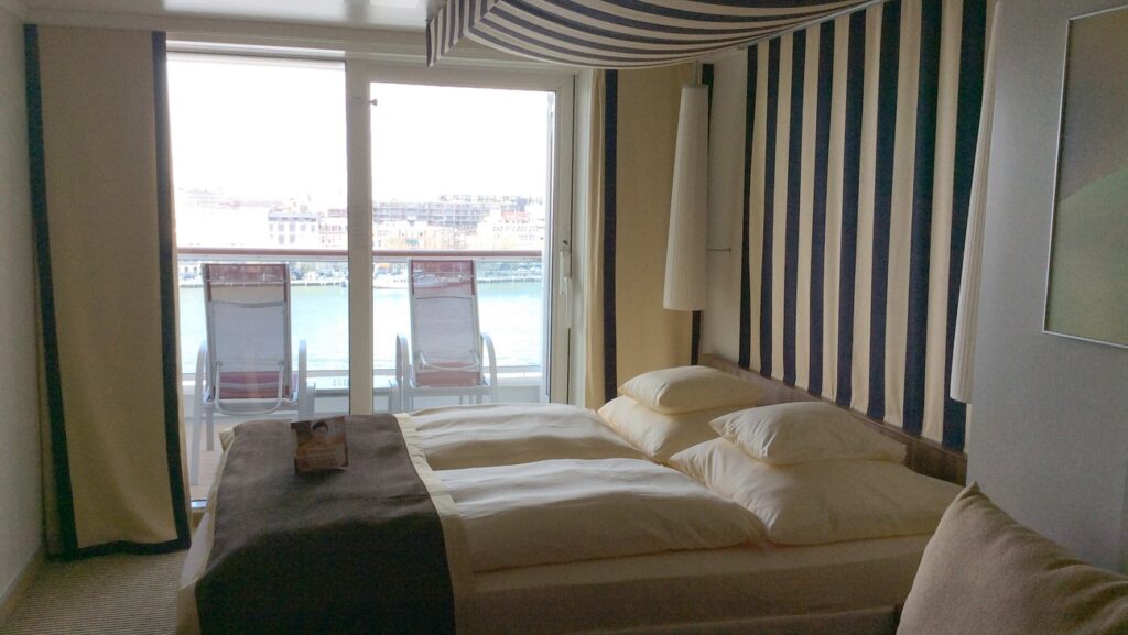 Balkonkabine auf der Aida Prima, mit einem Doppelbett, die Kabine ist gelb und braun gestaltet