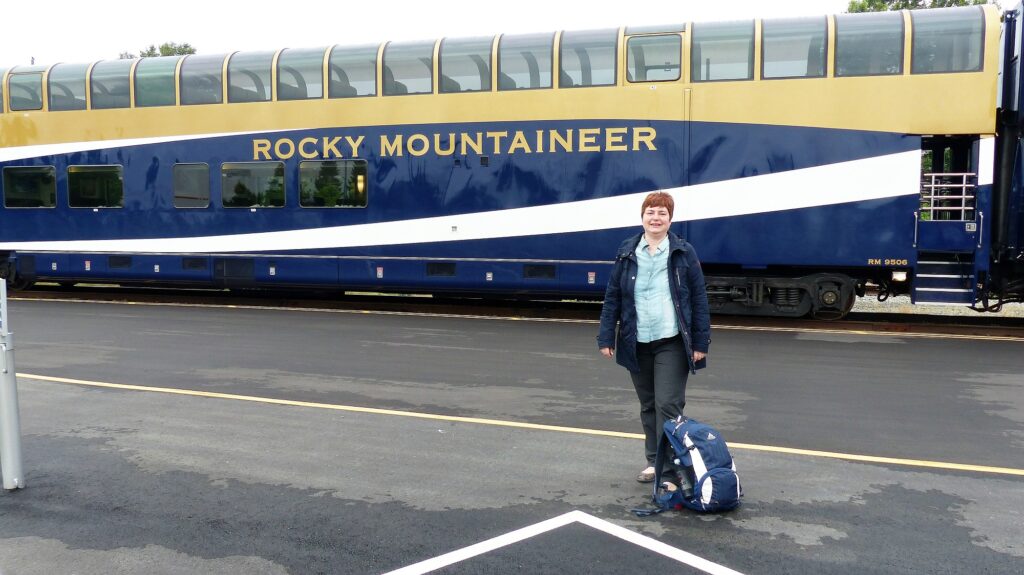 Mitarbeiterin Astrid Köhler posiert vor dem Rocky Mountaineer, einem zweistöckigem blau gelbem Zug