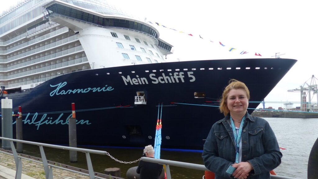 Mitarbeiterin Astrid Köhler posiert vor der Mein Schiff 5