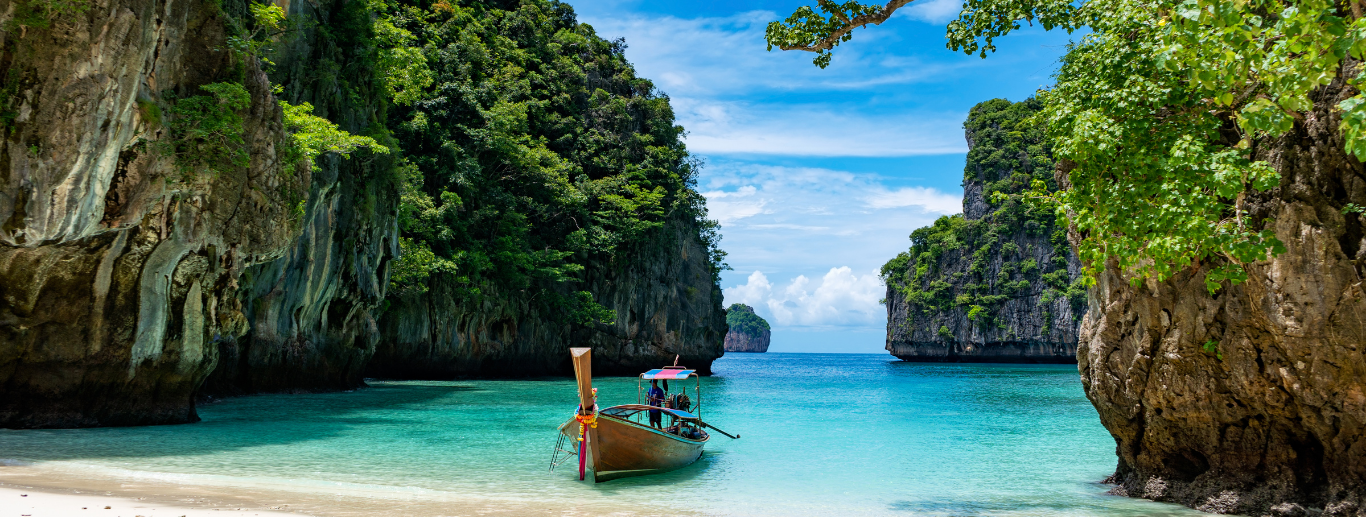 wunderschöner Strand in Thailand mit einem kleinen Boot und grünen Felsen drumherum