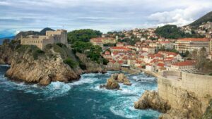 Blick auf eine Stadt an Klippen über dem Wasser, links eine Festung